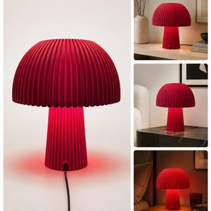 May include: A mushroom-shaped table lamp with a deep red, vertically ribbed shade and a matching cylindrical base. The lamp emits a vibrant red glow from beneath the shade and includes a black power cord extending from the base.