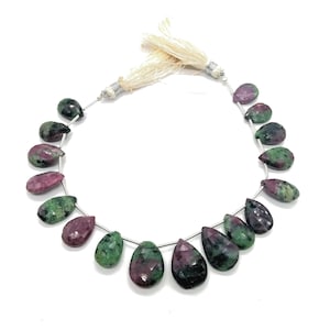 May include: A strand of teardrop-shaped beads. The beads are a mix of deep red and green, with a polished, smooth surface. The beads are strung on a thin, silver-coloured wire, and the strand is finished with a cream-coloured tassel.