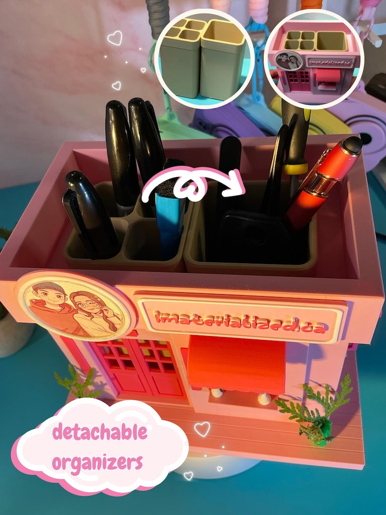 Peut inclure: Un organisateur de bureau rose en forme de petit magasin avec un portrait circulaire de deux personnes et du texte sur le devant. Il comporte plusieurs compartiments pour stylos et outils, dont deux organisateurs beiges d&eacute;tachables &agrave; l'int&eacute;rieur.
