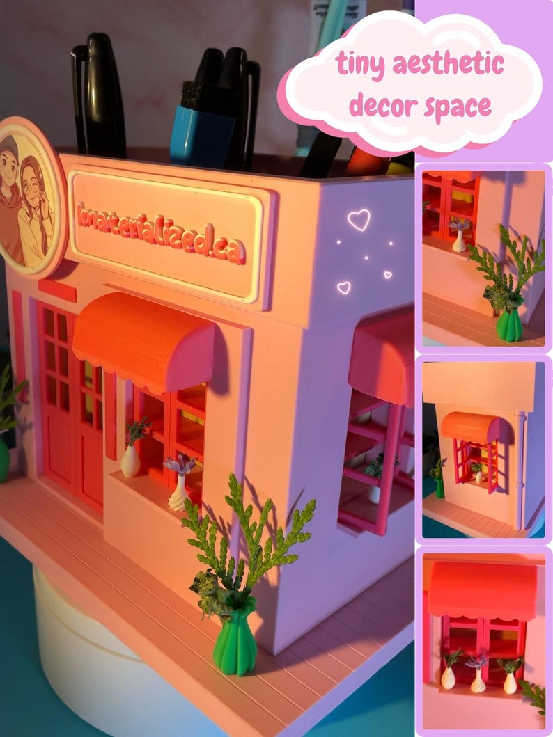 Peut inclure: Un organisateur de bureau rose en forme de boutique miniature avec des auvents orange, des cadres de fen&ecirc;tre rouges et une enseigne indiquant materialized.ca. Il comprend des petits vases blancs avec des plantes et des emplacements pour stylos.