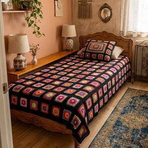 May include: A twin-sized bed featuring a black crochet blanket composed of numerous multi-colored granny squares in shades of pink, yellow, orange, and blue. A matching square crochet pillow sits at the head of the bed on a wooden frame.