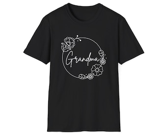 以下が含まれることがあります： 胸元に白い線画のグラフィックが施された黒の半袖Tシャツ。デザインは、筆記体フォントで書かれた「Grandma」という単語を囲む円形のフラワーリースで、小さな葉や花のモチーフがあしらわれています。