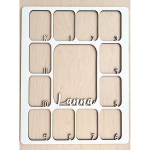May include: White wooden photo frame with 10 numbered slots for pictures. The frame has the name "Lanna" written in cursive on the bottom.