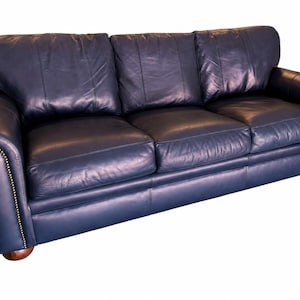 May include: A navy blue leather sofa with three seat cushions and three back cushions. The sofa has rolled arms with brass nailhead trim and sits on wooden feet. The leather has a slight sheen.