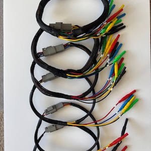 May include: A series of five circular electrical wiring harnesses, each featuring a grey plastic connector and black braided sleeving. Multiple individual wires in red, yellow, blue, green, and black extend from the harnesses, ending in small metal terminals.