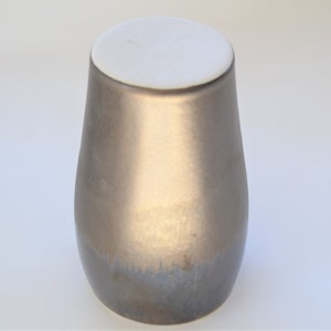 May include: A metallic gold ceramic vase with a white lid. The vase has a smooth, glossy finish and a rounded shape.