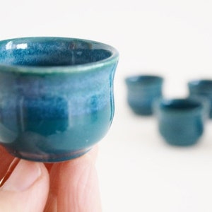 May include: A set of five small, teal blue ceramic cups. The cups are glazed and have a slightly rounded shape.