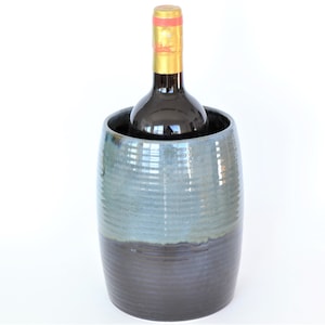 May include: A blue and black ceramic wine cooler with a bottle of wine inside.