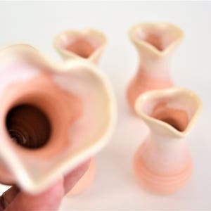 May include: Set of four small, heart-shaped ceramic vases in a light peach color with a white glaze. The vases are all slightly different in shape and size.