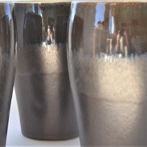 May include: Three ceramic mugs with a dark brown to light brown gradient glaze. The mugs are tall and cylindrical with a rounded bottom.