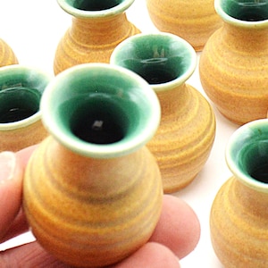 May include: A set of ten small, yellow ceramic vases with green glazed interiors. The vases are all the same size and shape, and they have a slightly rounded bottom.