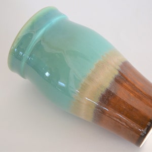 May include: A ceramic vase with a glossy finish. The top section is a light turquoise color, transitioning to a tan band, and then to a rich brown at the base. The vase has a slightly flared rim.
