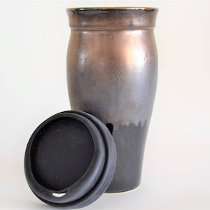May include: A ceramic travel mug with a black and copper glaze. The mug has a black silicone lid.
