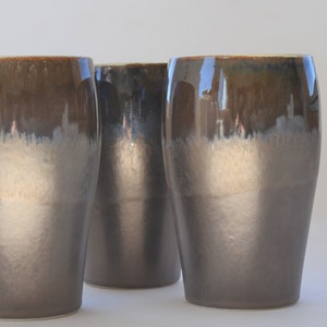 May include: Three ceramic mugs with a brown and gray glaze. The mugs have a rounded shape and a wide base.