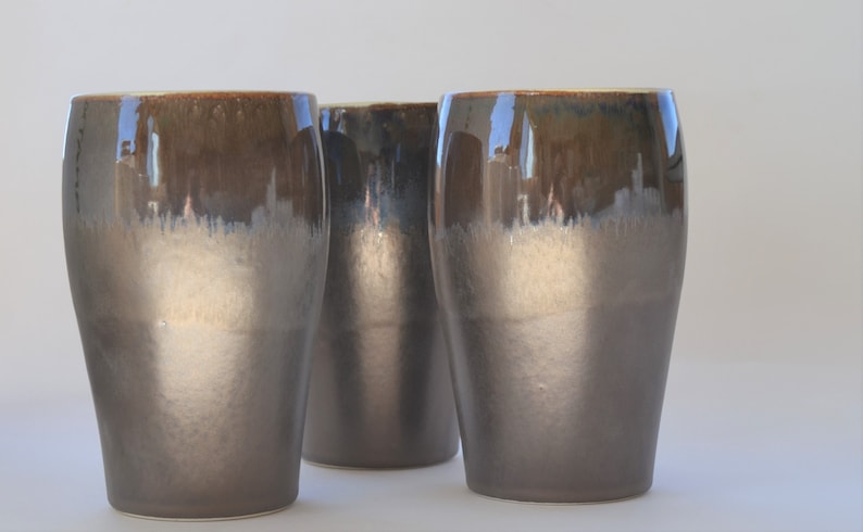 May include: Three ceramic mugs with a brown and gray glaze. The mugs have a rounded shape and a wide base.