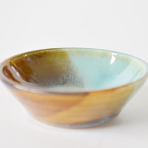 May include: A small, ceramic bowl with a brown, green, and blue glaze. The bowl is slightly flared at the top and has a rounded bottom.