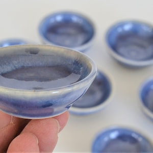 May include: A set of six small, blue ceramic bowls with a white rim. The bowls are glazed and have a subtle iridescent sheen.