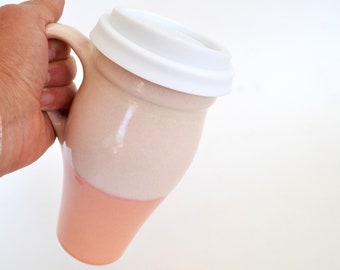 May include: A ceramic travel mug with a white lid and a two-tone design. The mug is white on top and peach on the bottom.