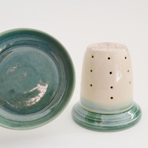 May include: A set of two ceramic dishes, one a small bowl with a green glaze and the other a taller, cylindrical container with a white glaze and a green band around the bottom. Both pieces have a speckled appearance.