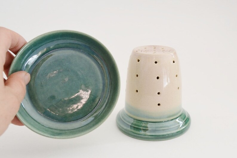 May include: A set of two ceramic dishes, one a small bowl with a green glaze and the other a taller, cylindrical container with a white glaze and a green band around the bottom. Both pieces have a speckled appearance.