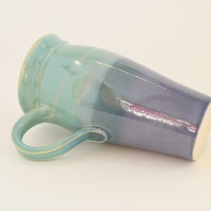 May include: A ceramic mug with a light blue to dark blue ombre glaze. The mug has a handle and a rounded shape.