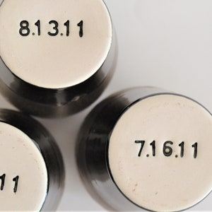May include: Three black ceramic mugs with white bottoms. Each mug has a black number printed on the bottom. The numbers are 8.13.11, 7.16.11, and 6.11.