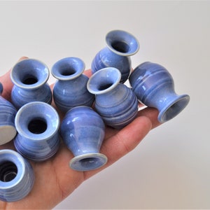 May include: A collection of ten small, blue and white ceramic vases. The vases are all different shapes and sizes, but they all have a similar blue and white glaze.