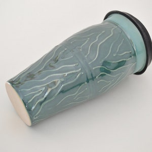 May include: A teal ceramic vase with a wavy pattern and a black rubber lid.