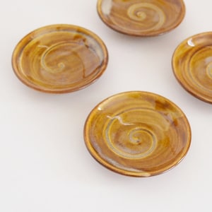 May include: Four small brown ceramic dishes with a swirl design. The dishes are on a white surface.