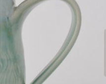 May include: Close-up of a light green ceramic teapot handle with a smooth, glazed finish.