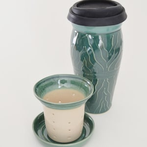 May include: A green ceramic tea infuser with a matching lid and a separate saucer. The infuser has a white interior and a pattern of green lines.