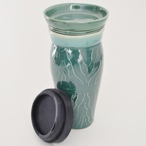 May include: A green ceramic travel mug with a black silicone lid. The mug has a wavy pattern and is stacked on top of two smaller green ceramic plates.