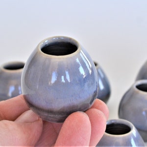 May include: A group of small, round, gray ceramic vases with a glossy finish. The vases are arranged in a semi-circle on a white surface.