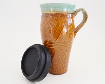 May include: A brown ceramic travel mug with a light blue rim and a black silicone lid. The mug has a geometric pattern.