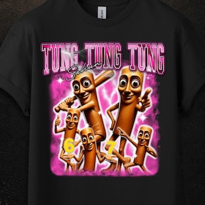 Op de afbeelding: Een zwart t-shirt met korte mouwen en een grafische print van vijf bruine, cilindervormige stripfiguren. De tekst TUNG TUNG TUNG staat in het roze erboven, met het woord Sahur en de gele cijfers 6 en 7 eronder.