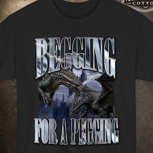 Könnte beinhalten: Schwarzes T-Shirt mit einer Grafik von zwei Drachen und dem Text "BEGGING FOR A PEGGING" in einem reflektierenden, metallischen Stil. Das Shirt enthält das "Midnight Cotton" Logo.