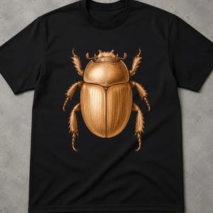 Pode incluir: Uma t-shirt preta de manga curta com uma ilustração grande e detalhada de um escaravelho castanho-dourado centrada no peito. O gráfico do escaravelho apresenta um trabalho intrincado de linhas e sombreamento, destacando o seu corpo segmentado, patas e asas.