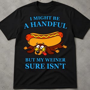 Könnte beinhalten: Ein schwarzes Kurzarm-T-Shirt mit einer Grafik eines braunen Dackels, der eine gelbe Sonnenbrille trägt und ein Hot-Dog-Brötchen auf dem Rücken hat. Der Text lautet I MIGHT BE A HANDFUL BUT MY WEINER SURE ISN'T in hellblauen Großbuchstaben.
