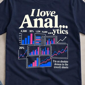 Può includere: Una t-shirt a maniche corte blu navy con il testo bianco I love Anal...ytics. La grafica include vari grafici a barre e a linee colorati nelle tonalità del blu e del rosa, con il testo aggiuntivo I'm an absolute demon in the (excel) sheets.
