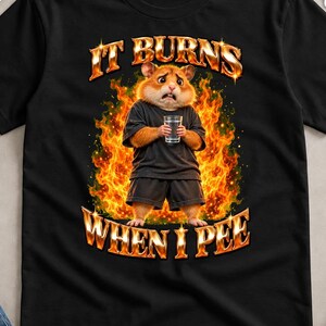 Könnte beinhalten: Ein schwarzes T-Shirt mit einer Grafik eines Hamsters, der ein schwarzes T-Shirt und eine kurze Hose trägt, ein Glas Wasser hält und von Flammen umgeben ist. Der Text "IT BURNS" steht über dem Hamster, "WHEN I PEE" darunter in Flammenschrift.