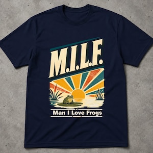 Könnte beinhalten: Ein kurzärmeliges T-Shirt in Marineblau mit einem Grafikdruck eines grünen Frosches auf einem Seerosenblatt bei Sonnenuntergang. Über dem Frosch steht M.I.L.F. in großen cremefarbenen Buchstaben, darunter Man I Love Frogs in Weiß.