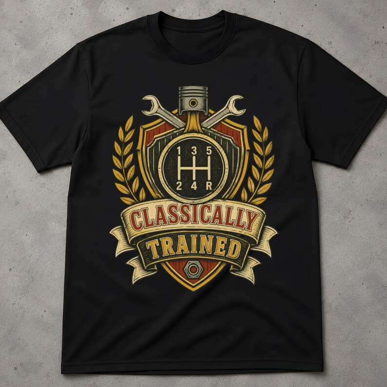 May include: A black short-sleeve t-shirt featuring a graphic print of a shield with a manual transmission gear shift pattern, a piston, two wrenches, and wheat stalks. The text "CLASSICALLY TRAINED" is printed on a banner across the centre.
