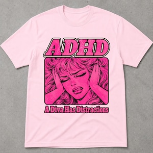May include: A light pink short-sleeve t-shirt featuring a graphic print of a person with hands on their head. The text "ADHD" appears in large letters above the graphic, and the text "A Diva Has Distractions" is printed in black below the image.