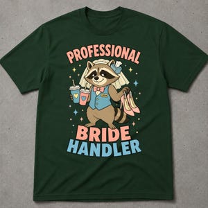 Puede incluir: Una camiseta de manga corta verde oscuro con un mapache de dibujos animados que lleva un chaleco azul, pajarita y velo de novia. El mapache sostiene dos bebidas y tacones rosas. El texto dice: PROFESSIONAL BRIDE HANDLER.