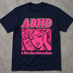 Può includere: Una t-shirt blu navy a maniche corte con una stampa grafica rosa. Il design include il testo "ADHD" in alto, un'illustrazione in stile manga di una persona che tiene un "DIARY" al centro e il testo "A Diva Has Distractions" nella parte inferiore.