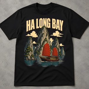 Può includere: Una t-shirt nera a maniche corte con una stampa grafica della baia di Ha Long. Il design mostra alti faraglioni calcarei, una giunca tradizionale con vele rosse sull'acqua e il testo HA LONG BAY in grandi lettere maiuscole chiare.