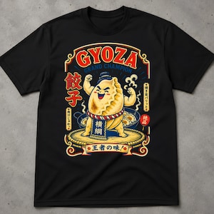 Może przedstawiać: Czarny t-shirt z krótkim rękawem z grafiką umięśnionego pierożka gyoza przebranego za zapaśnika sumo. Wzór zawiera napis GYOZA GRAND CHAMPION, japońskie znaki oraz parującą patelnię z pierożkami w formie kolorowej i szczegółowej ilustracji.