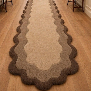 May include: A long runner rug with a scalloped edge. The rug has a layered design in shades of brown, from light tan to dark chocolate. The rug is placed on a wooden floor.