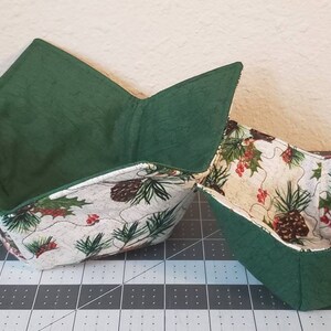 May include: Two green fabric bowls with a white and green pine tree print. The bowls are folded flat and are ready to be used.