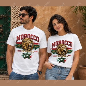 May include: White t-shirts with a graphic design featuring the word "MOROCCO" in maroon, a roaring lion, and the words "FOOTBALL" and "الأطلس أسود". The design includes a green star and red and green stripes.